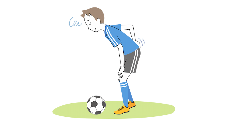 サッカーのユニフォームを着た高校生が、腰を痛そうにさすりながら腰をくの字に曲げている。