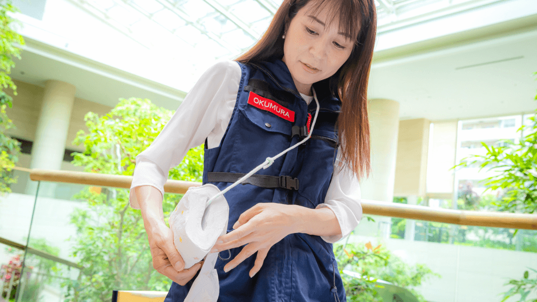 トイレットペーパーを通した紐を肩から斜め掛けしている奥村さん