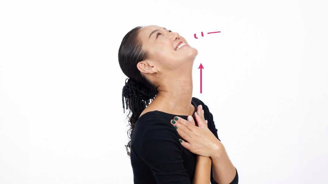 両手をクロスさせた状態で鎖骨に置き、あごを持ち上げて首を伸ばし、口を「いー」の形にしている写真