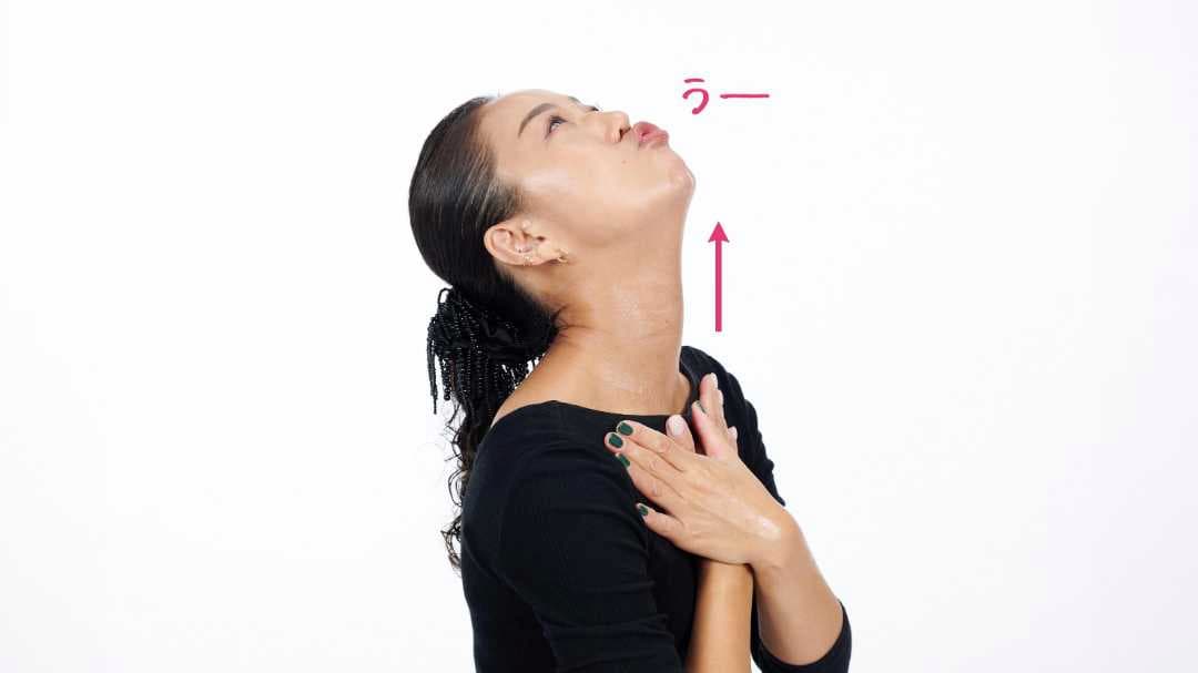両手をクロスさせた状態で鎖骨に置き、あごを持ち上げて首を伸ばし、口を「うー」の形にしている写真